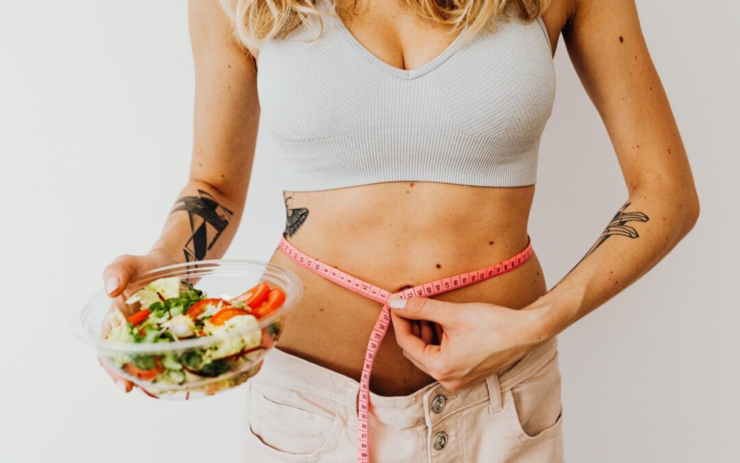 woman measuring waist using tape while holding bowl of salad